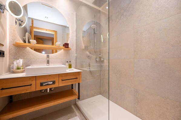 A modern bathroom with a freestanding sink, a glass shower enclosure, and a vanity with a mirror and shelves. - Übergossene Alm Resort (Dienten am Hochkoenig)