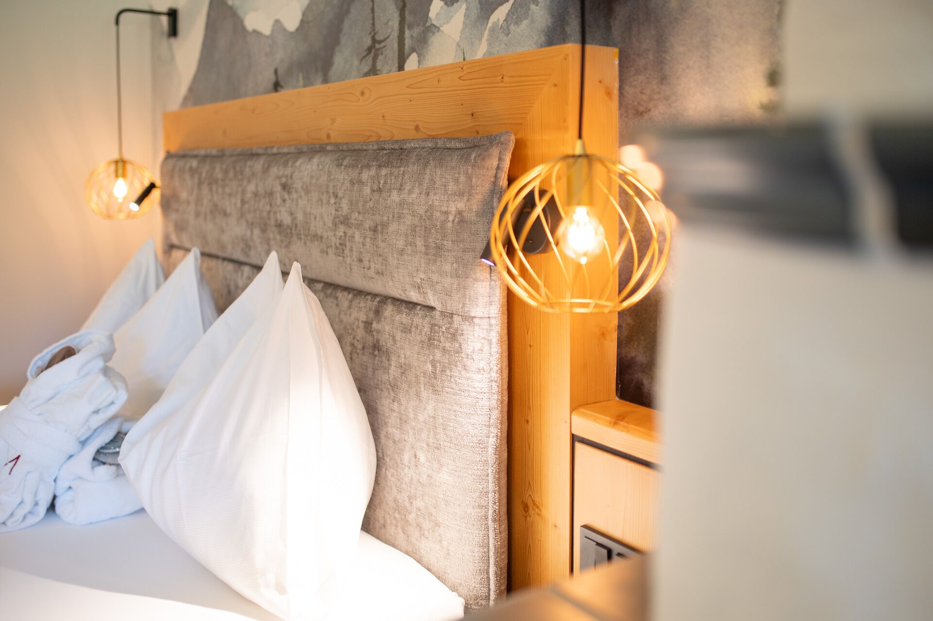 Een bed met witte kussens en een houten hoofdbord. Er hangen twee hanglampen met zichtbare gloeilampen.
