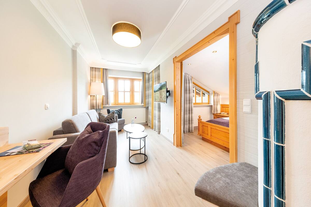 A spacious living area with a sofa, a coffee table, and a dining table with magazines. A staircase leads to an upper level with a bed and a window.