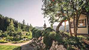 Un jardín ajardinado con un sendero, un estanque y un edificio con vistas a montañas.
