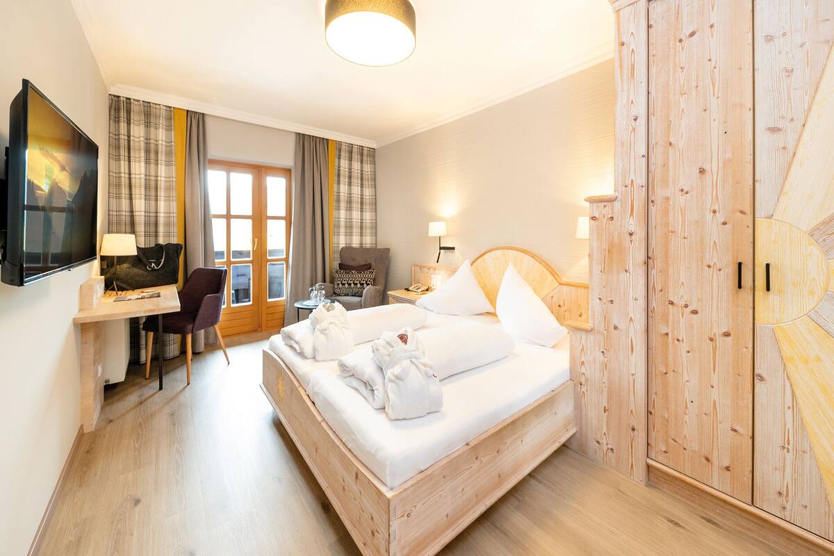 A hotel room with a bed, a desk, a chair, a TV, and a wardrobe.