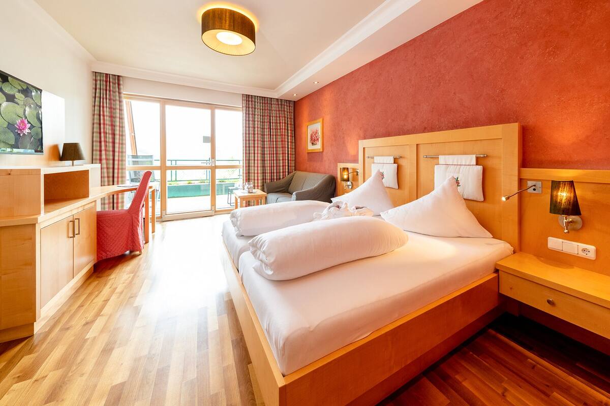 A hotel room with a large bed, a desk, a chair, and a view of the outdoors.