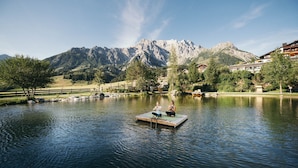 Un lago sereno con dos personas meditando sobre una plataforma flotante, rodeado de montañas y una valla de madera.