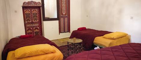 Una habitación con dos camas, cada una con una colcha roja y amarilla, una pequeña mesa redonda con una bandeja y un espejo decorativo en la pared.
