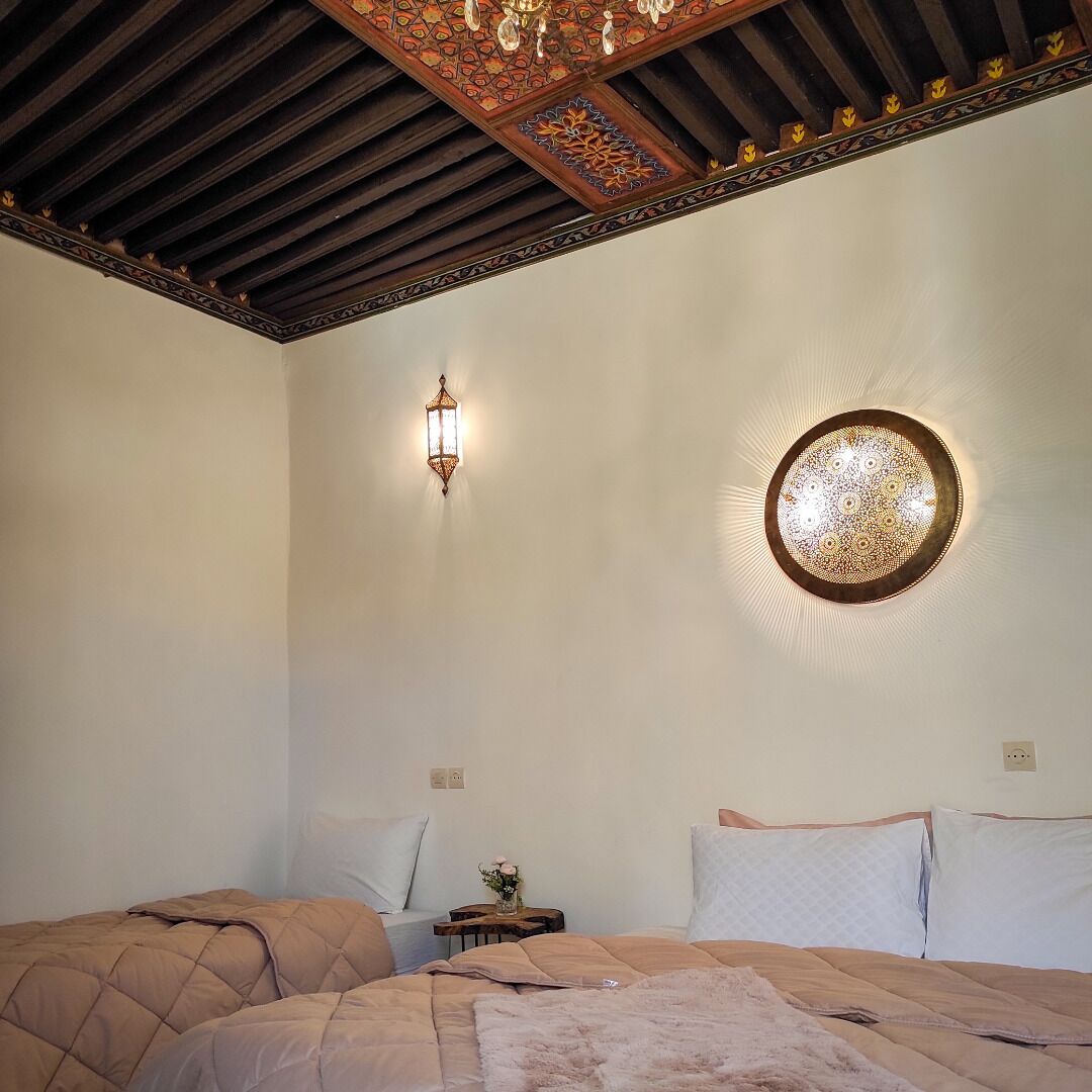 Une chambre avec deux lits, un plafond décoratif et un luminaire fixé au mur.