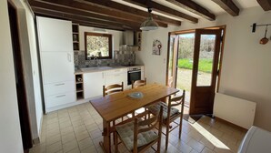 A kitchen with a wooden table and chairs, a window, and a door leading outside. - Country house in the heart of rural Pays d'Auge (Le Renouard)