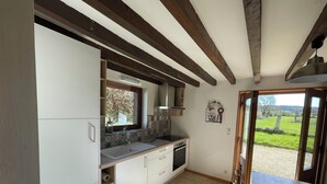 A kitchen with white cabinets, a window, and a view of a green field. - Country house in the heart of rural Pays d'Auge (Le Renouard)