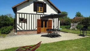 A traditional half-timbered house with a gravel patio, a wooden door, and a small table with chairs. - Country house in the heart of rural Pays d'Auge (Le Renouard)