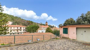 Un pati empedrat amb un edifici que té teules vermelles i una petita construcció amb una persiana verda.