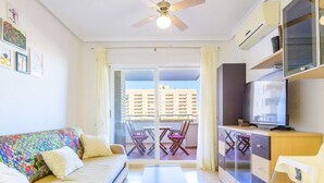 A modern living room with a sofa, a coffee table, a TV, and a balcony with a view of buildings. - Jardines del Mar I by Interhome (Oropesa del Mar)
