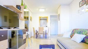 A modern living room with a sofa, a TV, a dining area with chairs, and a kitchen in the background. - Jardines del Mar I by Interhome (Oropesa del Mar)