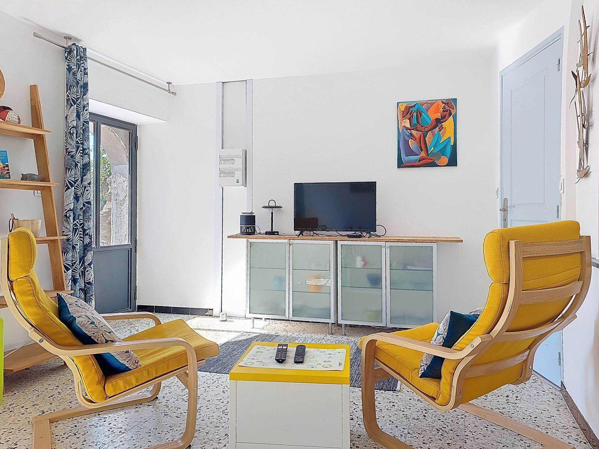 Una sala de estar con dos sillones amarillos, un televisor sobre un mueble y un cuadro en la pared.