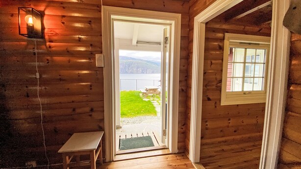 A wooden cabin interior with a door leading to a balcony overlooking a lake.