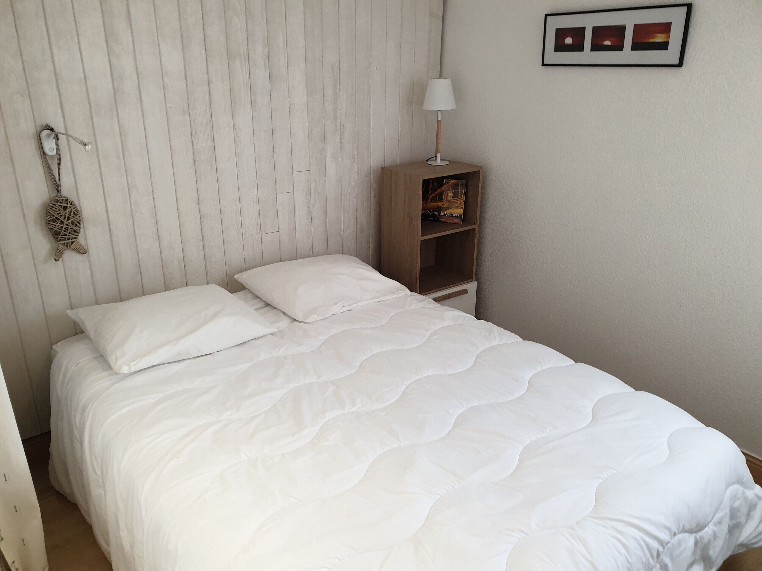 A neatly made bed with white bedding in a room with a wooden headboard and a small wooden nightstand with a lamp.