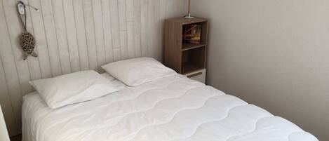 A neatly made bed with white bedding in a room with a wooden headboard and a small wooden nightstand with a lamp.