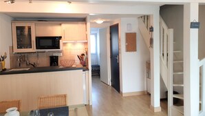 A modern kitchen with a microwave, stove, and cabinets. There is a dining area with a table and chairs. A staircase leads to another level. - GARENNE - Holiday apartment for rent in Carnac - T23 (Carnac)