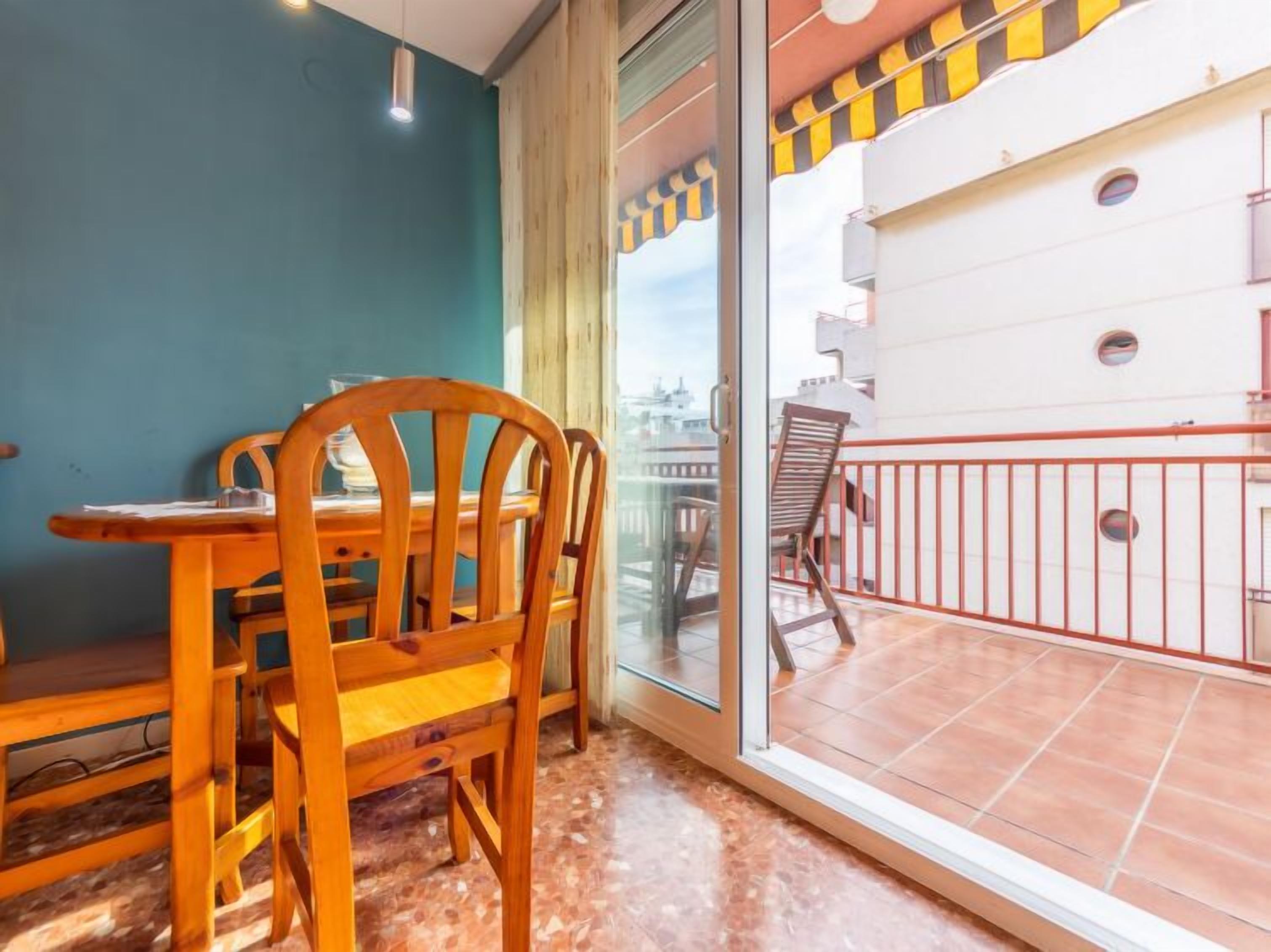 A room with a wooden dining table and chairs, a glass door leading to an outdoor balcony with a red railing.