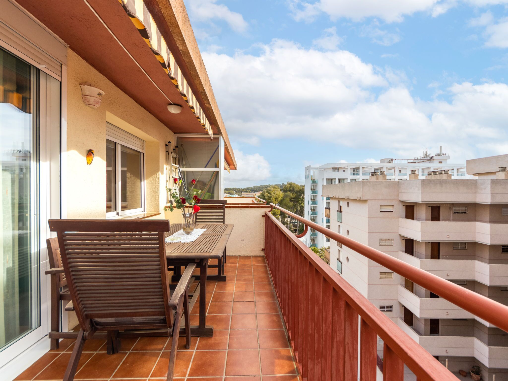 Ein Balkon mit Holztisch und -stühlen, einer Blumenvase und Blick auf umliegende Gebäude.