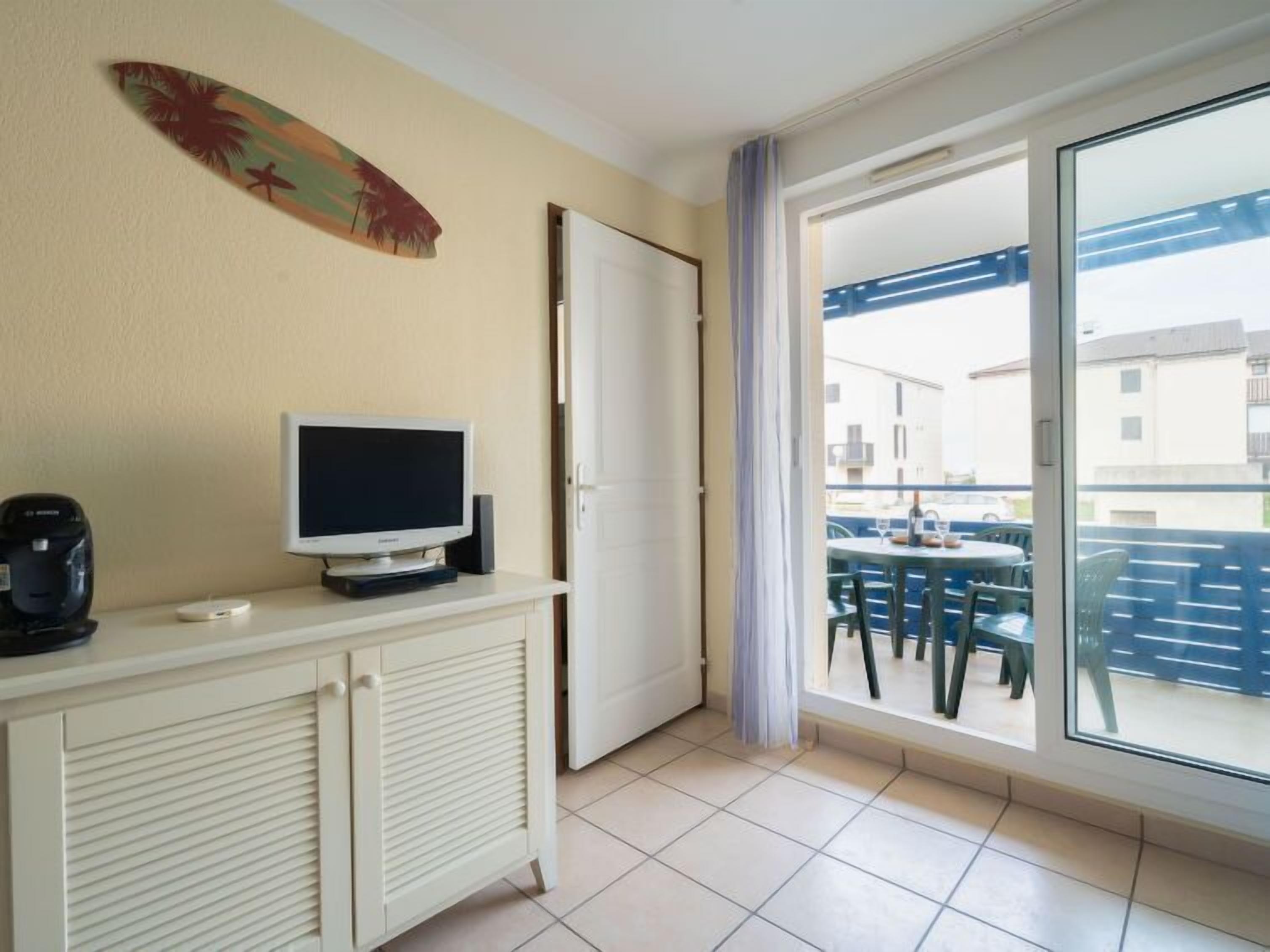 Ein Zimmer mit Fernseher auf einer Kommode, einer Schiebetür zum Balkon und einem Surfbrett als Wanddekoration.