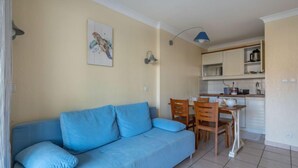 A living room with a blue sofa and a dining area with wooden chairs and a small table. - Bleu Marine by Interhome (Lacanau)