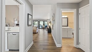 A hallway with a kitchen area on the left, a living room with a sofa and chairs in the center, and a bathroom with a sink and mirror on the right. - Modern, Cozy, & Quiet - Sea Pines, Near Beach (Hilton Head Island)