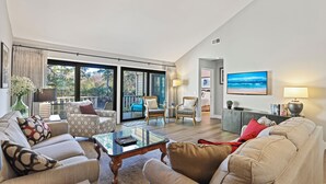 A spacious living room with a large glass door leading to a balcony, a comfortable sofa set, a coffee table, and a TV. - Modern, Cozy, & Quiet - Sea Pines, Near Beach (Hilton Head Island)