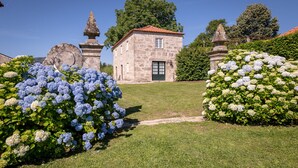 A stone building with a tiled roof, surrounded by well-maintained hedges and a clear pathway leading to the entrance. - Casa de Luou ground floor at Quinta de Luou (Ponte de Lima)