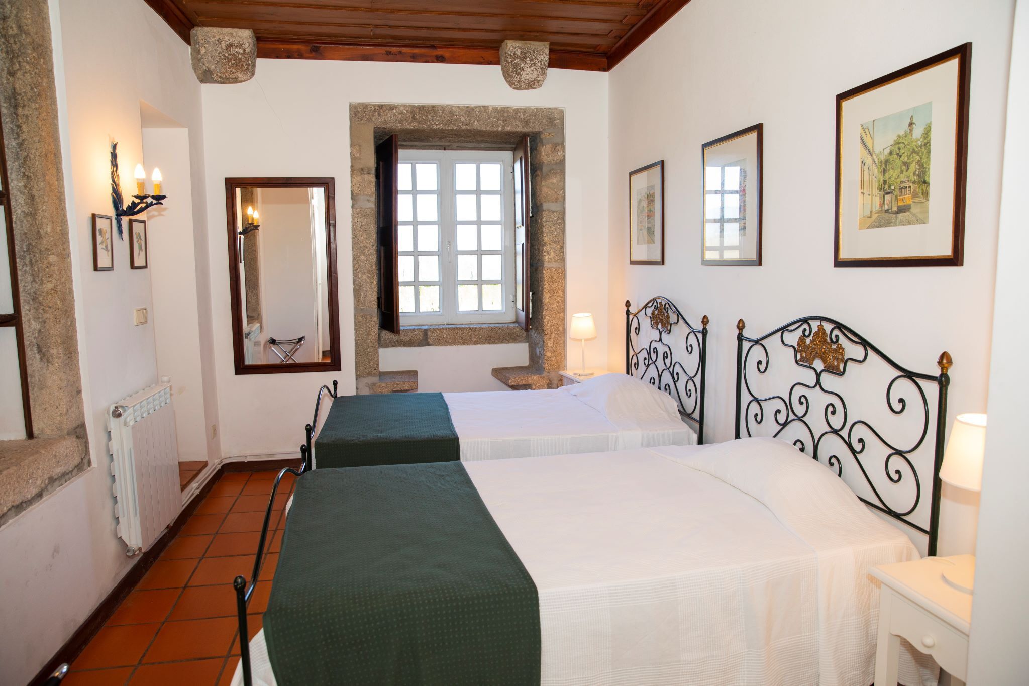 Ein Zimmer mit zwei Betten, einem Fenster mit Steinrahmen, einer Heizung und gerahmten Kunstwerken an den Wänden.