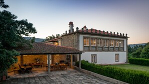 A traditional stone building with a tiled roof, a patio with outdoor furniture, and a well-maintained garden. - Casa de Luou ground floor at Quinta de Luou (Ponte de Lima)