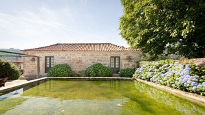 A stone building with a tiled roof, a small pond, and a row of hydrangea bushes. - Casa do Tanque at Quinta de Luou (Ponte de Lima)