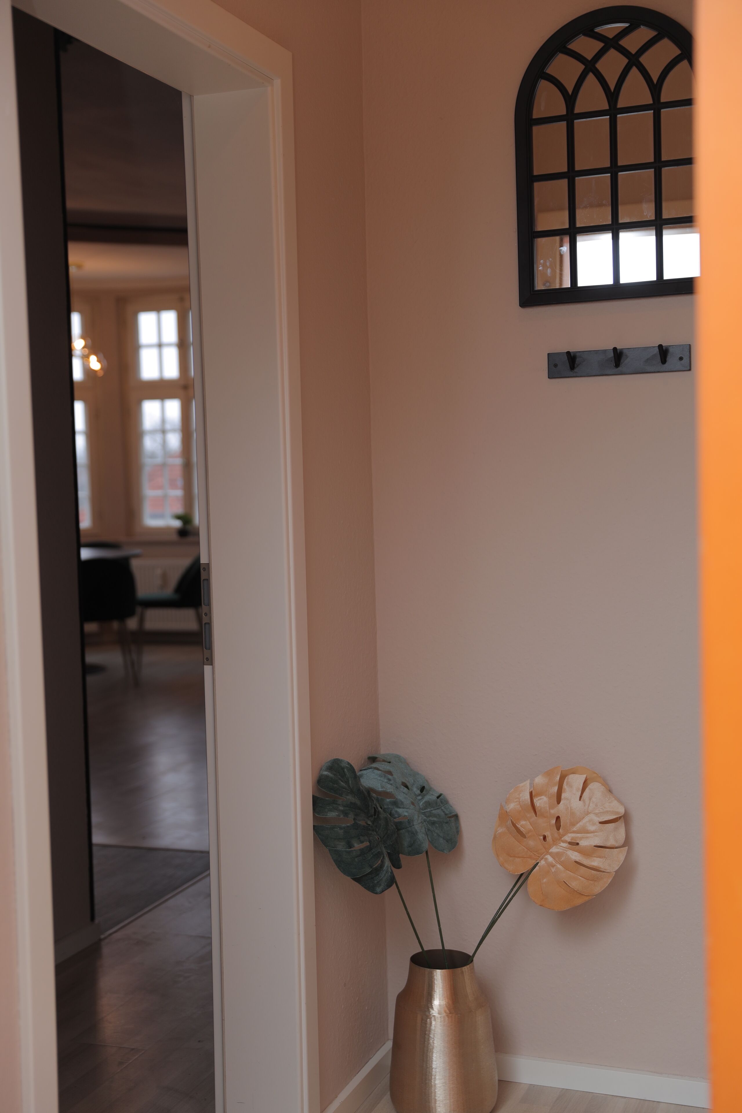 Een hal met een bloemenvaas op de muur, een deur naar een andere kamer, en een raam met decoratieve lijst.