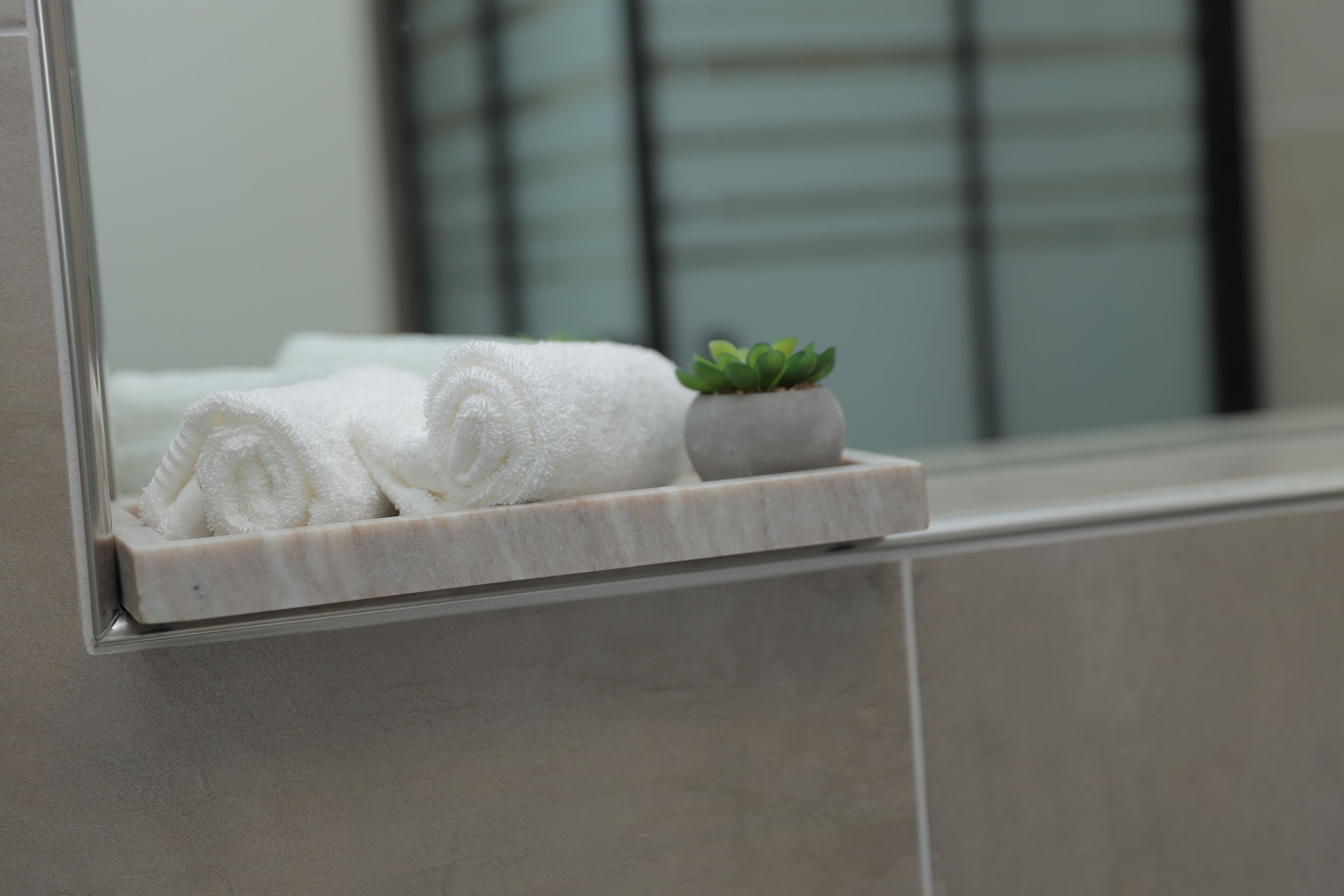 A bathroom with a marble sink, a towel rack with rolled towels, and a small potted plant.
