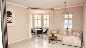 A spacious living room with a large beige sofa, a round coffee table, and a dining area with a table and chairs.