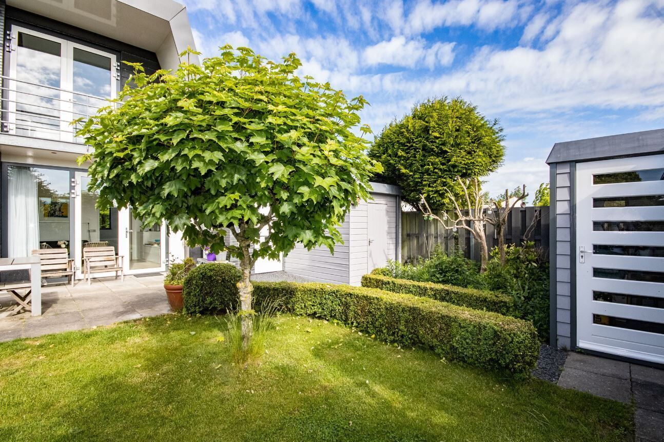 Une maison moderne avec un jardin bien entretenu, un grand arbre et une clôture blanche.