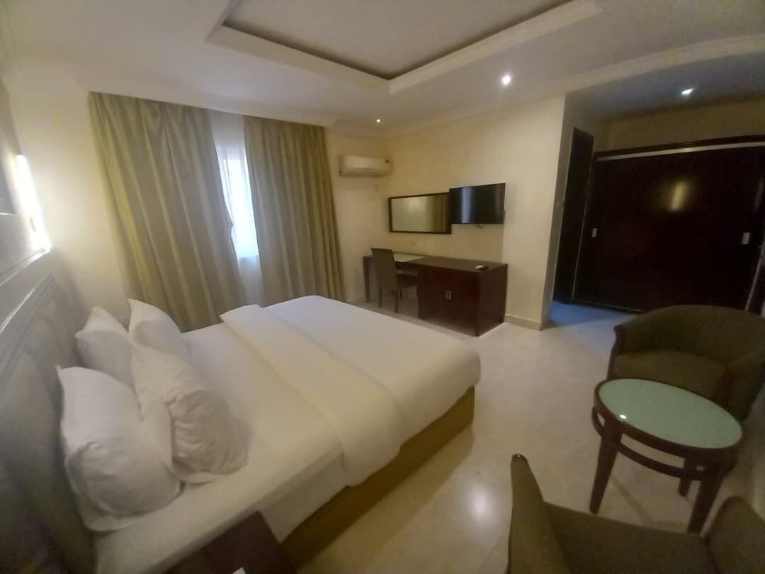 A hotel room with a bed, a desk, a chair, a television, and a wardrobe.