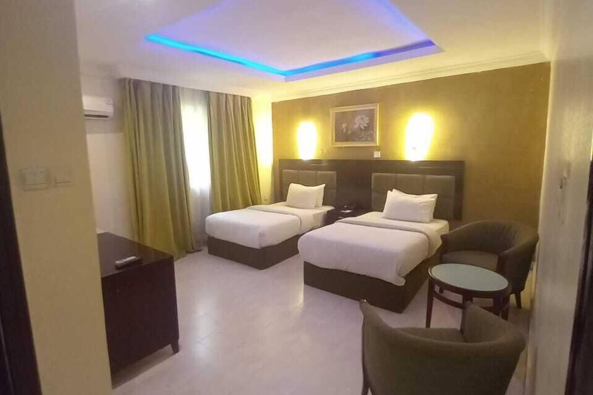 A hotel room with two beds, a desk, a chair, and a small table.