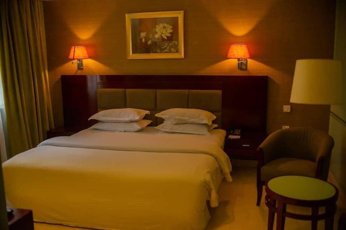 A hotel room with a large bed, two bedside lamps, a chair, and a small table.