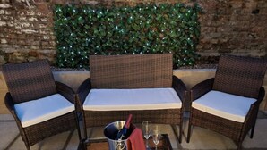 Um conjunto de sofás de vime com almofadas, uma mesa de vidro com uma garrafa e copos, e uma parede decorativa com folhagem.