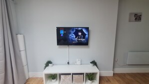 Uma sala de estar moderna com uma TV fixada na parede exibindo um pôster de filme, um console branco com plantas decorativas e uma parede de tijolos.
