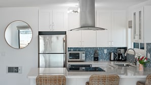 Une cuisine moderne avec des meubles blancs, des appareils en acier inoxydable, un îlot central doté de tabourets de bar et un crédence bleue carrelée.