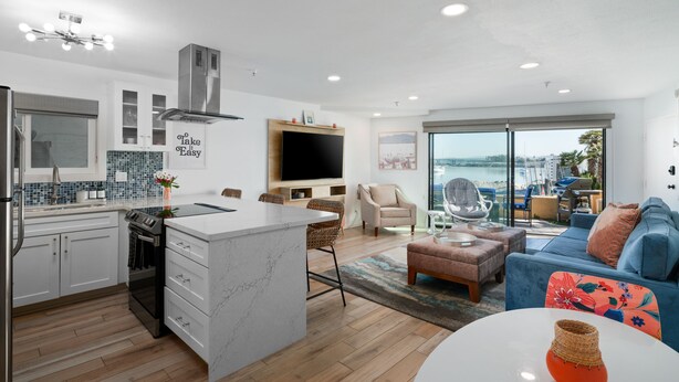 Une cuisine moderne avec un îlot central, un coin repas équipé d’un téléviseur et un salon avec un canapé et vue sur la mer.