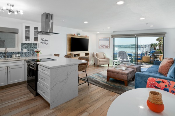 Bay Views- Living room with smart TV, comfortable couch and 2 lounge chairs. Kitchen with bar seating, 2-person dining table, and electric stove/range.