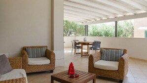 Ein überdachter Patio-Bereich mit Korbmöbeln, einem Tisch mit einer roten Laterne und Blick ins Grüne.