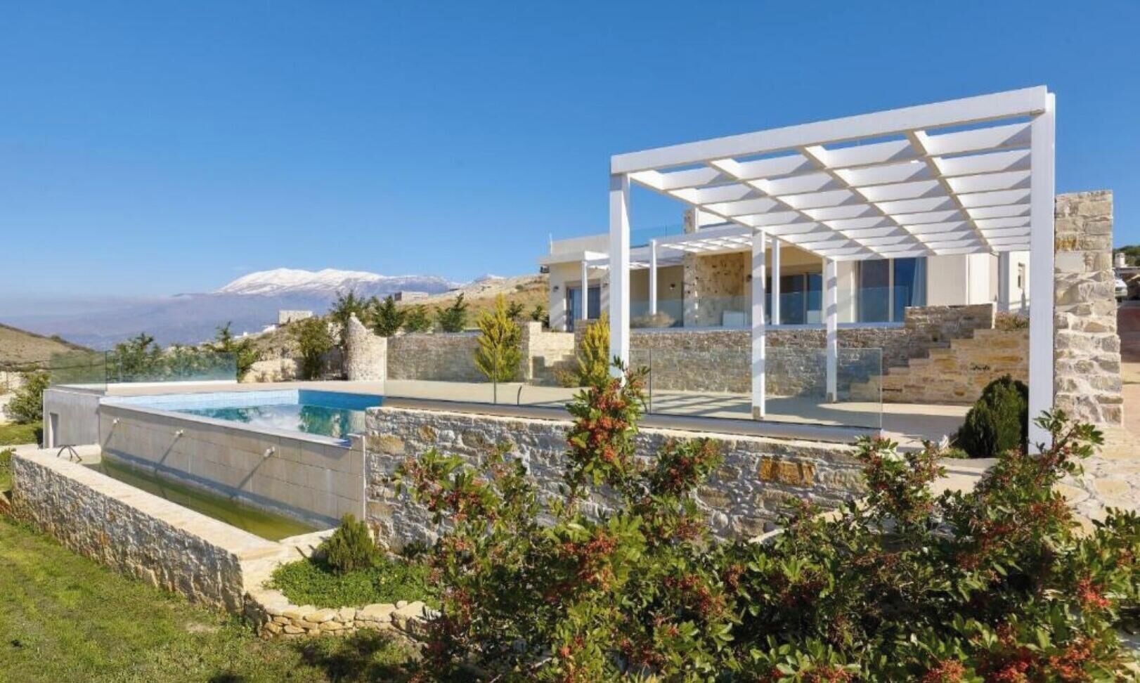 A modern house with a pool, stone walls, and a view of snow-capped mountains.