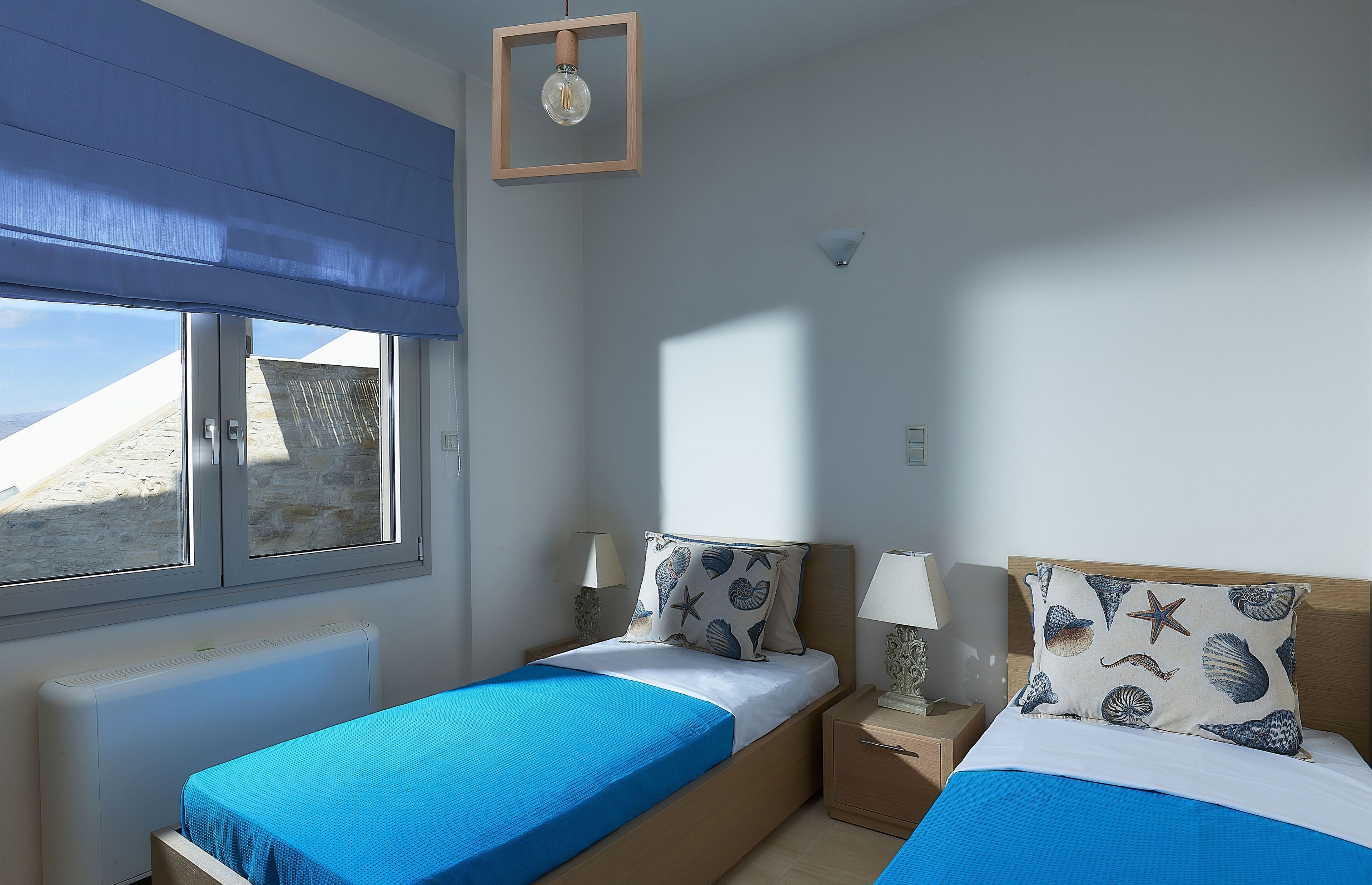 A bedroom with two beds, a view of the beach, and a window with a blue blind.