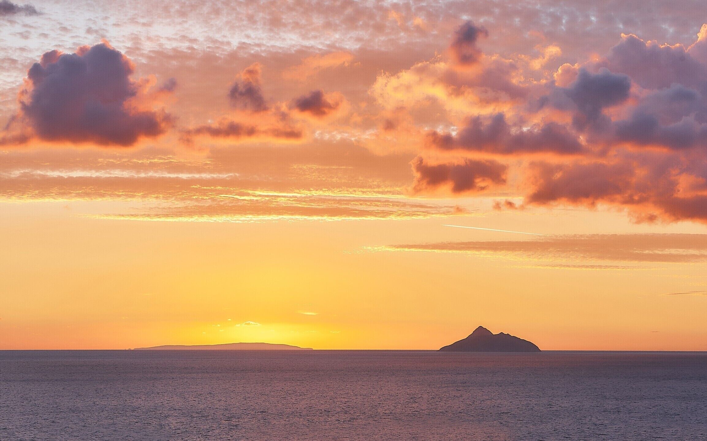 Ein Sonnenuntergang über einem ruhigen Meer mit der Silhouette einer fernen Insel.