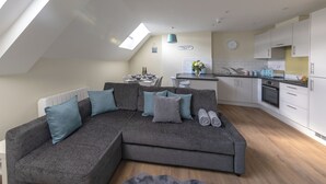 En modern lägenhet i loftstil med en grå hörnsoffa, en matplats och ett kök.