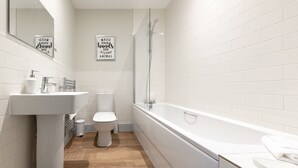 Ett modernt badrum med ett vitt handfat, en toalett och ett badkar. Det finns två skyltar på väggen, en ovanför handfatet och en ovanför badkaret.
