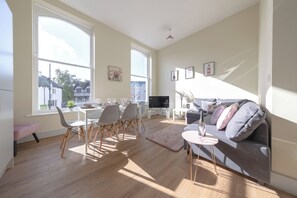 Ett modernt vardagsrum med en matplats, stora fönster, en platt-TV och en grå soffa.