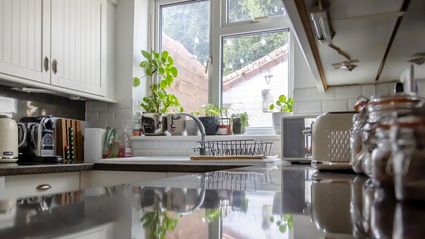 A kitchen with white cabinets, a stainless steel countertop, and a window with a view of a red-roofed building. - HEREFORD CITY – St Owens Terrace: Spacious 3-Storey Home, Walk to Centre (Hereford)